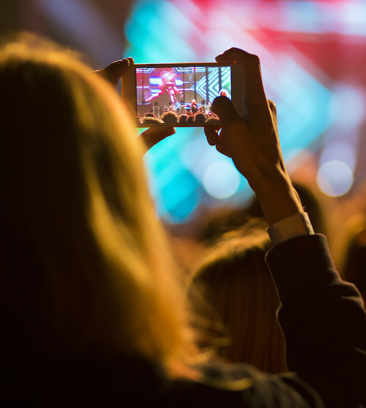 A content creator filming a live music concert for YouTube through her smart phone.